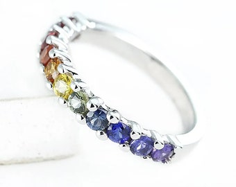 May include: A silver band ring with a rainbow of gemstones. The stones are set in a row around the band and are in the order of red, orange, yellow, green, blue, indigo, and violet.