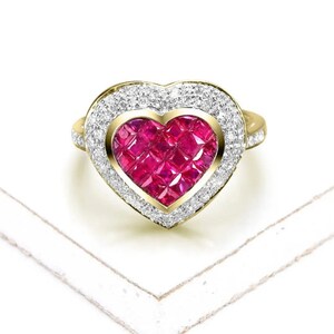 May include: A gold heart-shaped ring with a large ruby centre surrounded by a halo of smaller diamonds.