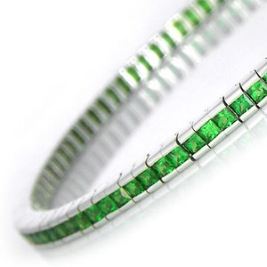 Puede incluir: Una pulsera de plata con una fila de piedras preciosas verdes cuadradas.