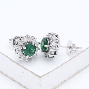 May include: A pair of silver earrings with a green gemstone surrounded by smaller white gemstones.