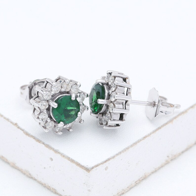 May include: A pair of silver earrings with a green gemstone surrounded by smaller white gemstones.