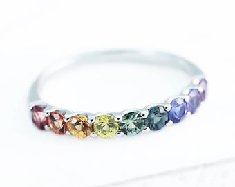 May include: A silver band ring with a rainbow of gemstones. The stones are set in a row and are in the colors red, orange, yellow, green, blue, and purple.