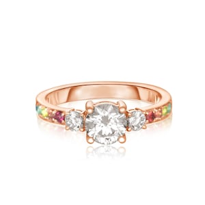 Puede incluir: Un anillo de oro rosa con una gran piedra central redonda y dos piedras redondas más pequeñas a cada lado. La banda está engastada con una fila de piedras preciosas de colores.