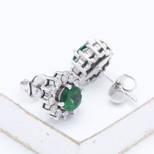 May include: A pair of silver earrings with a green gemstone surrounded by smaller white gemstones.