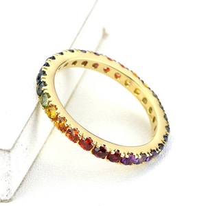 Puede incluir: Un anillo de banda de oro con un arcoíris de piedras preciosas engastadas en una línea continua alrededor de la banda.