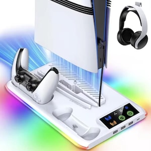 Puede incluir: Una estación de carga y refrigeración blanca para consola de juegos con iluminación RGB integrada. La base cuenta con ranuras para una consola, dos mandos y un soporte para auriculares. Incluye un panel de control digital con iconos de ventilador y luz, además de varios puertos USB.