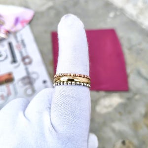 May include: A stack of three rings worn on a finger covered by a white glove. The top ring is rose gold with a beaded texture, the middle ring is smooth yellow gold, and the bottom ring is silver with a beaded texture, creating a tri-colour set.