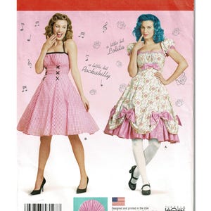 May include: Simplicity sewing pattern 8127 for sizes 8-16. The envelope features two dress designs: a pink gingham dress with black lacing and a floral print dress with puff sleeves and pink bows. Text includes "a little bit Lolita" and "a little bit Rockabilly."
