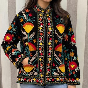 May include: A black jacket featuring a mandarin collar and long sleeves, decorated with vibrant multi-colored floral embroidery in shades of red, yellow, orange, and teal. The jacket includes two front pockets and a straight hemline.