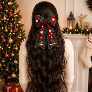 Könnte beinhalten: Eine dunkelrote Häkel-Haarschleife mit zwei langen Bändern, verziert mit weißen gestickten Schneeflocken, grün-weißen Weihnachtsbaummotiven und einer zentralen Gruppe aus drei kleinen roten Beeren mit grünen Blättern, alles dunkelgrün umrandet.