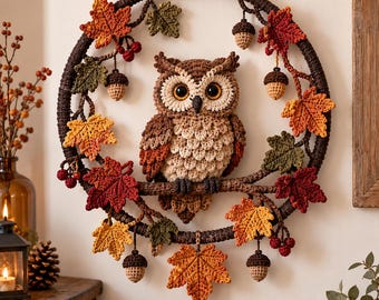 May include: A circular wall hanging featuring a crocheted brown owl perched on a branch within a dark brown ring. The piece is decorated with crocheted autumn leaves in shades of red, orange, and green, along with small crocheted acorns and berries.