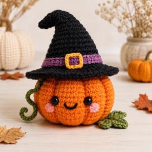 May include: A crocheted orange pumpkin wearing a black witch hat with a purple band and a yellow buckle. The pumpkin features two black bead eyes, a stitched black smile, and pink cheeks. It has a green curly vine and a green leaf attached.