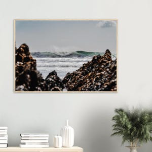 Puede incluir: Una impresión de arte mural de paisaje enmarcada que muestra olas del océano rompiendo entre dos grandes formaciones rocosas oscuras y texturizadas. La escena captura la espuma blanca del oleaje contra un cielo nublado y agua azul.