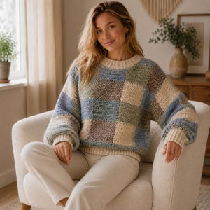 May include: A long-sleeved sweater featuring a large checkered pattern in shades of blue, green, brown, and cream. The garment has a ribbed crew neckline and ribbed cuffs in a solid cream color, with a textured knit construction throughout.