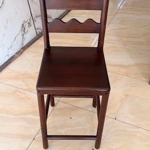 May include: A dark brown wooden chair featuring a square seat and a backrest composed of two horizontal slats with a scalloped, wavy edge design. The chair has four straight legs connected by horizontal support bars on the sides and front.
