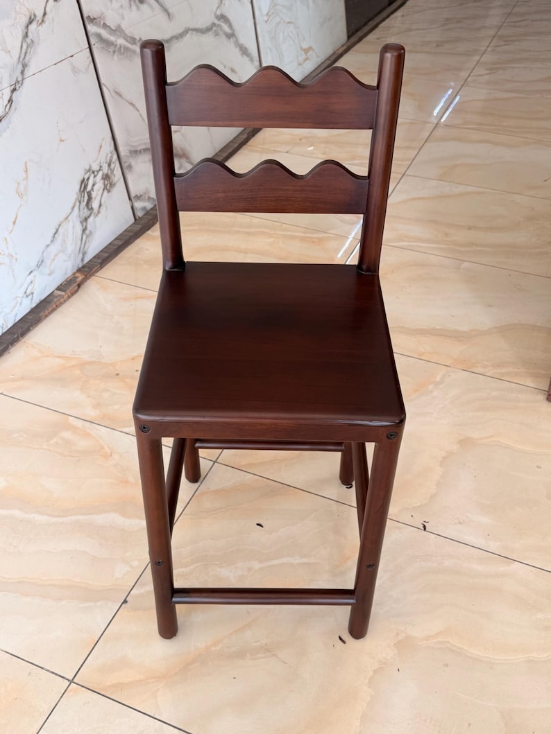 May include: A dark brown wooden chair featuring a square seat and a backrest composed of two horizontal slats with a scalloped, wavy edge design. The chair has four straight legs connected by horizontal support bars on the sides and front.