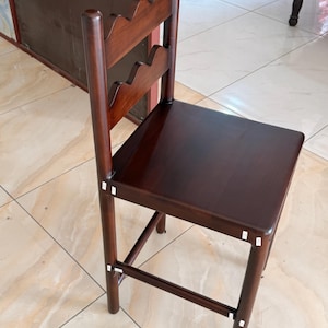 May include: A dark brown wooden chair featuring a square seat and a backrest with two horizontal slats, each designed with a scalloped, wavy top edge. The chair has four straight legs connected by horizontal support bars on the sides and front.