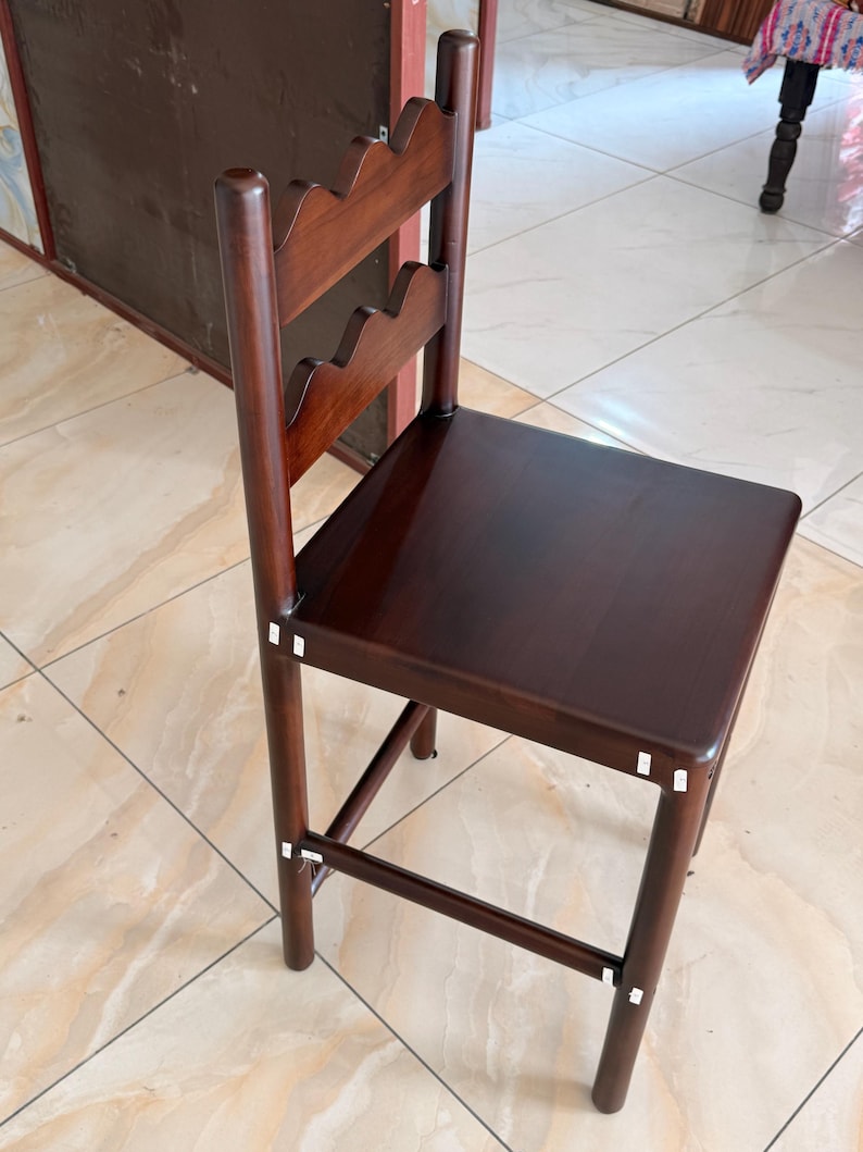 May include: A dark brown wooden chair featuring a square seat and a backrest with two horizontal slats, each designed with a scalloped, wavy top edge. The chair has four straight legs connected by horizontal support bars on the sides and front.
