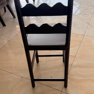 May include: A dark brown wooden chair featuring a high backrest with two horizontal slats, each designed with a scalloped, wavy top edge. The chair has four straight legs connected by horizontal support bars on the sides and front.