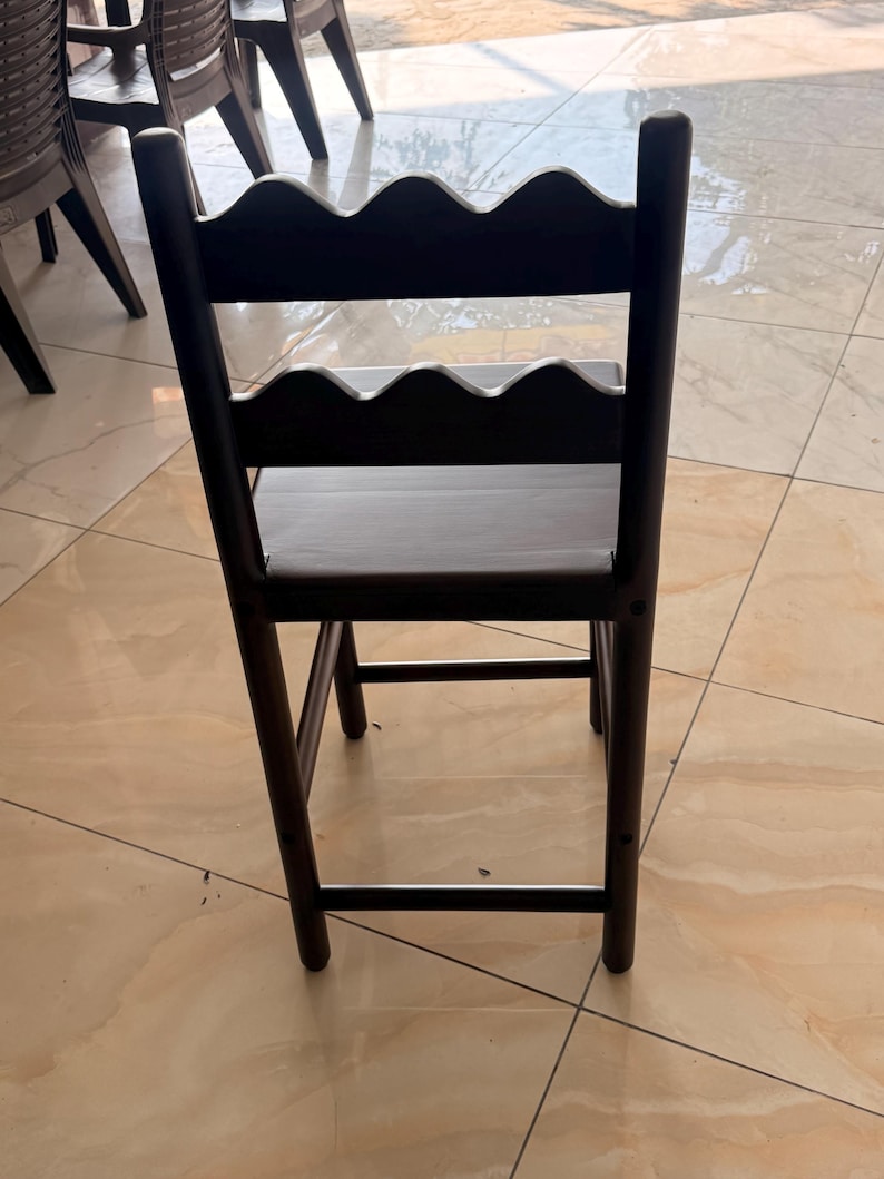 May include: A dark brown wooden chair featuring a high backrest with two horizontal slats, each designed with a scalloped, wavy top edge. The chair has four straight legs connected by horizontal support bars on the sides and front.