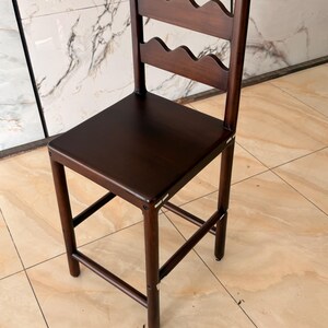 May include: A dark brown wooden bar stool featuring a square seat and a backrest composed of two horizontal slats with a scalloped, wavy edge design. The stool has four straight legs connected by horizontal support bars on all four sides.