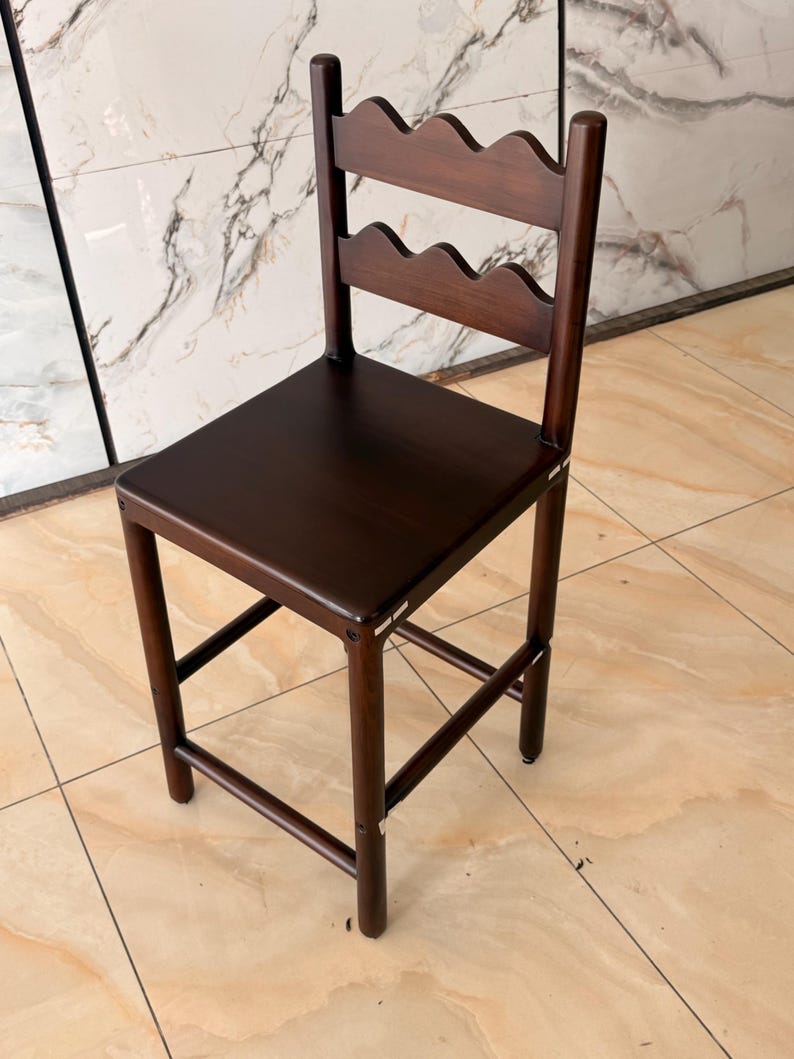 May include: A dark brown wooden bar stool featuring a square seat and a backrest composed of two horizontal slats with a scalloped, wavy edge design. The stool has four straight legs connected by horizontal support bars on all four sides.