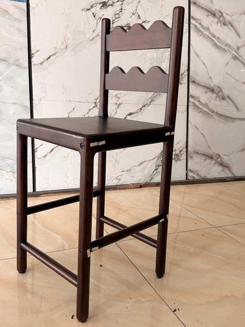 May include: A dark brown wooden bar stool featuring a square seat and a backrest composed of two horizontal slats with a scalloped, wavy edge design. The stool has four straight legs connected by horizontal support bars on all four sides.