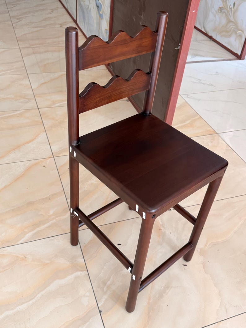May include: A dark brown wooden bar stool featuring a square seat and a backrest with two horizontal slats, each designed with a scalloped top edge. The stool has four straight legs connected by horizontal support bars on all four sides.
