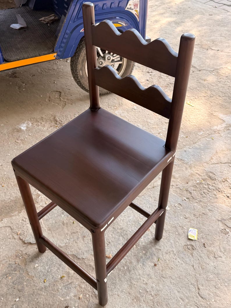 May include: A dark brown wooden bar stool featuring a square seat and a backrest with two horizontal slats, each designed with a scalloped, wavy top edge. The stool is supported by four straight legs connected by horizontal rungs for stability.