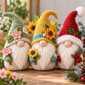 Puede incluir: Tres gnomos de ganchillo con largas barbas blancas y gorros puntiagudos. El primer gorro es verde con flores rosas, el segundo es amarillo con un girasol y el tercero es rojo con un pompón blanco, hojas de acebo verdes y bayas rojas.