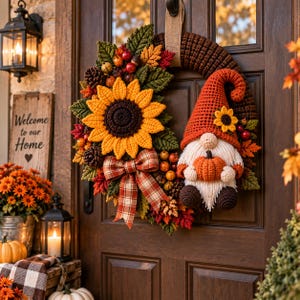 Könnte beinhalten: Ein dekorativer Herbstkranz mit einer großen gehäkelten Sonnenblume, einem Zwerg mit orangefarbener Mütze und kleinem Kürbis, gehäkelten grünen Blättern, Tannenzapfen, roten Beeren und einer karierten Schleife an einer dunkelbraunen Tür.