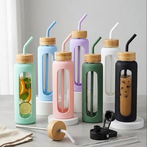May include: A collection of glass water bottles with bamboo lids and silicone sleeves in various colors including mint, blue, pink, purple, green, white, and black. Each bottle features a matching silicone straw and a clear window to view contents.