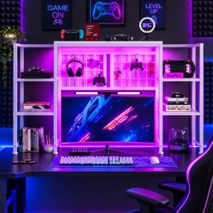 May include: A white multi-tiered gaming desk hutch with integrated LED lighting, featuring a central grid panel for hanging accessories, side shelving for storage, and a monitor stand. The setup includes a curved monitor, keyboard, and mouse.