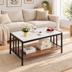 May include: A rectangular coffee table with a white faux marble top and a dark brown wooden lower shelf, supported by a black metal frame. The table holds a vase of white daisies, a white mug, a small bowl of red apples, and two stacked books.