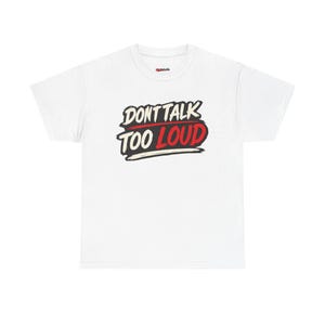 May include: A white short-sleeved t-shirt featuring a graphic print on the chest. The design displays the text "DONT TALK" in black and "TOO LOUD" in red, set against a stylised black brushstroke background with white highlights and a clean crew neck.