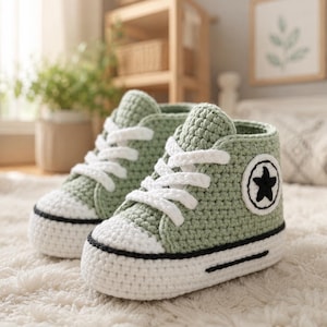 Op de afbeelding: Een paar gehaakte high-top sneakers in saliegroen met witte veters, witte neuzen in rubberstijl en een zwarte rand langs de zool. Elke schoen heeft een ronde witte patch aan de zijkant met een zwart sterembleem in het midden.