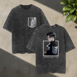 May include: A charcoal grey acid-wash t-shirt featuring a white Scout Regiment emblem on the front chest. The back displays a graphic of the character Levi Ackerman in a black uniform with the text ATTACK ON TITAN printed in white below.