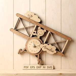 May include: A wooden wall clock shaped like a biplane featuring a central clock face, a cutout of a person with pigtails, a bird on a cloud, and a cloud engraved with the name Amelia. The text PDF EPS DXF AI SVG is printed below.