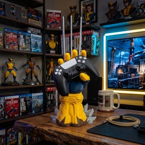 May include: A yellow and blue glove-shaped controller stand featuring three long silver claws extending from the knuckles, holding a black and white wireless game controller. The base is yellow with sculpted rock details at the bottom.