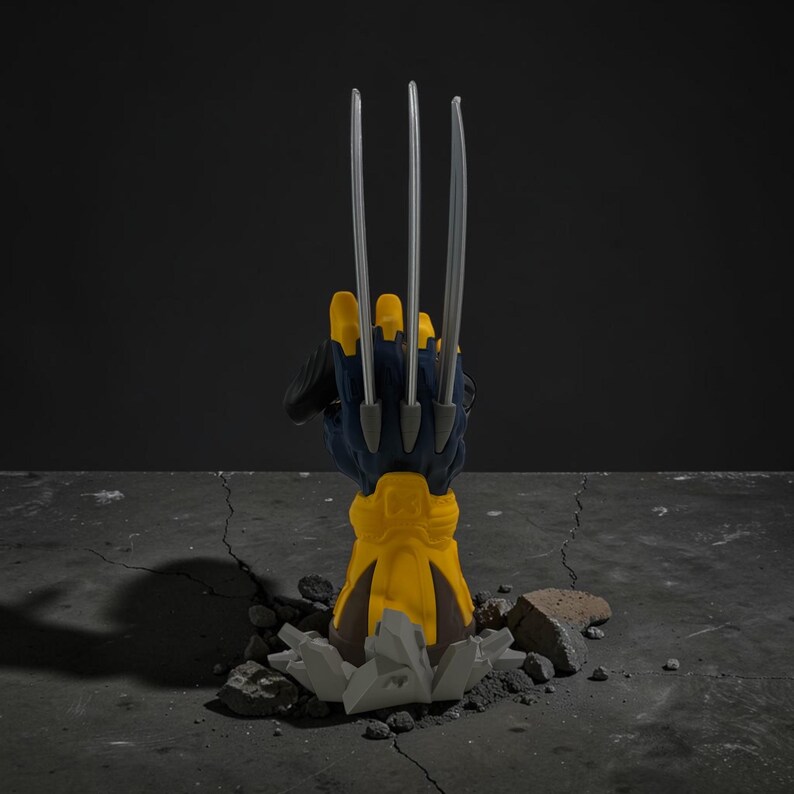 May include: A yellow and dark blue sculpted hand figurine featuring three long, sharp silver-colored claws extending upward. The base of the hand is encased in a yellow gauntlet, emerging from a cracked, gray, rocky-textured ground surface.