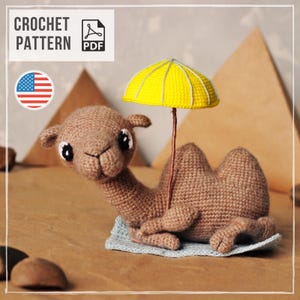May include: A brown crocheted camel toy with large black and white eyes, resting on a light blue crocheted mat. The camel holds a small yellow crocheted umbrella with white ribs. The image includes text reading CROCHET PATTERN PDF.