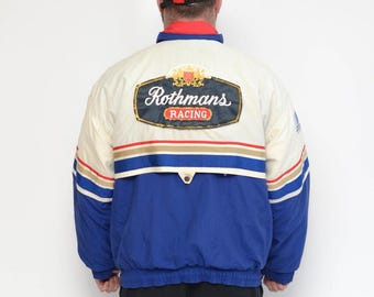May include: A color-blocked jacket featuring a cream upper section and a blue lower section, separated by red, white, and gold horizontal stripes. A large patch on the back displays the text Rothmans RACING with a crest logo.