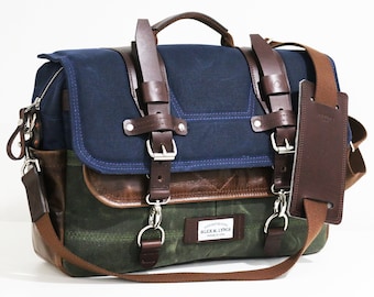 May include: A blue and green canvas messenger bag with brown leather accents and straps. The bag has a buckle closure and a small leather patch with the text "ALBERT & LYNCH" on it.