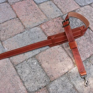 May include: A brown leather guitar strap with two metal clasps. The strap is adjustable and has a wide, padded section for comfort.
