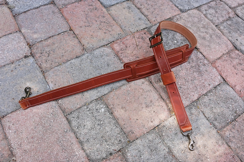 May include: A brown leather guitar strap with two metal clasps. The strap is adjustable and has a wide, padded section for comfort.
