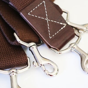 May include: Three brown canvas straps with silver metal clasps. The straps are connected to a brown leather strap with white stitching.