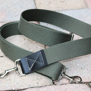 May include: A green canvas camera strap with black leather accents and silver metal clasps.