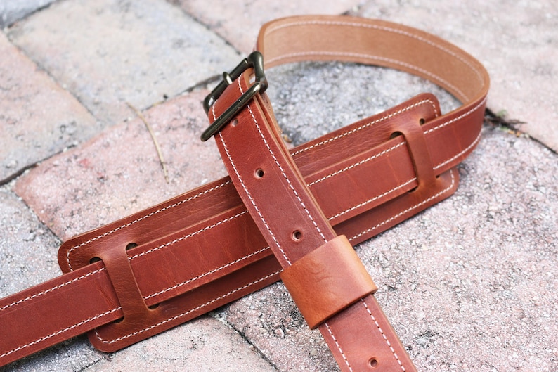 May include: A brown leather guitar strap with white stitching and a metal buckle. The strap is folded in half and the buckle is visible.