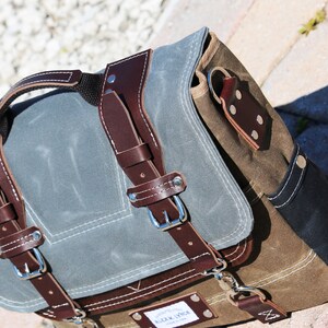 May include: A brown and gray canvas messenger bag with leather straps and buckles. The bag has a flap closure and a small pocket on the front. The bag is made by "Alex & Sons".
