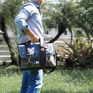 May include: A blue and brown canvas messenger bag with a leather strap and buckle closures. The bag has a front pocket and a large main compartment.
